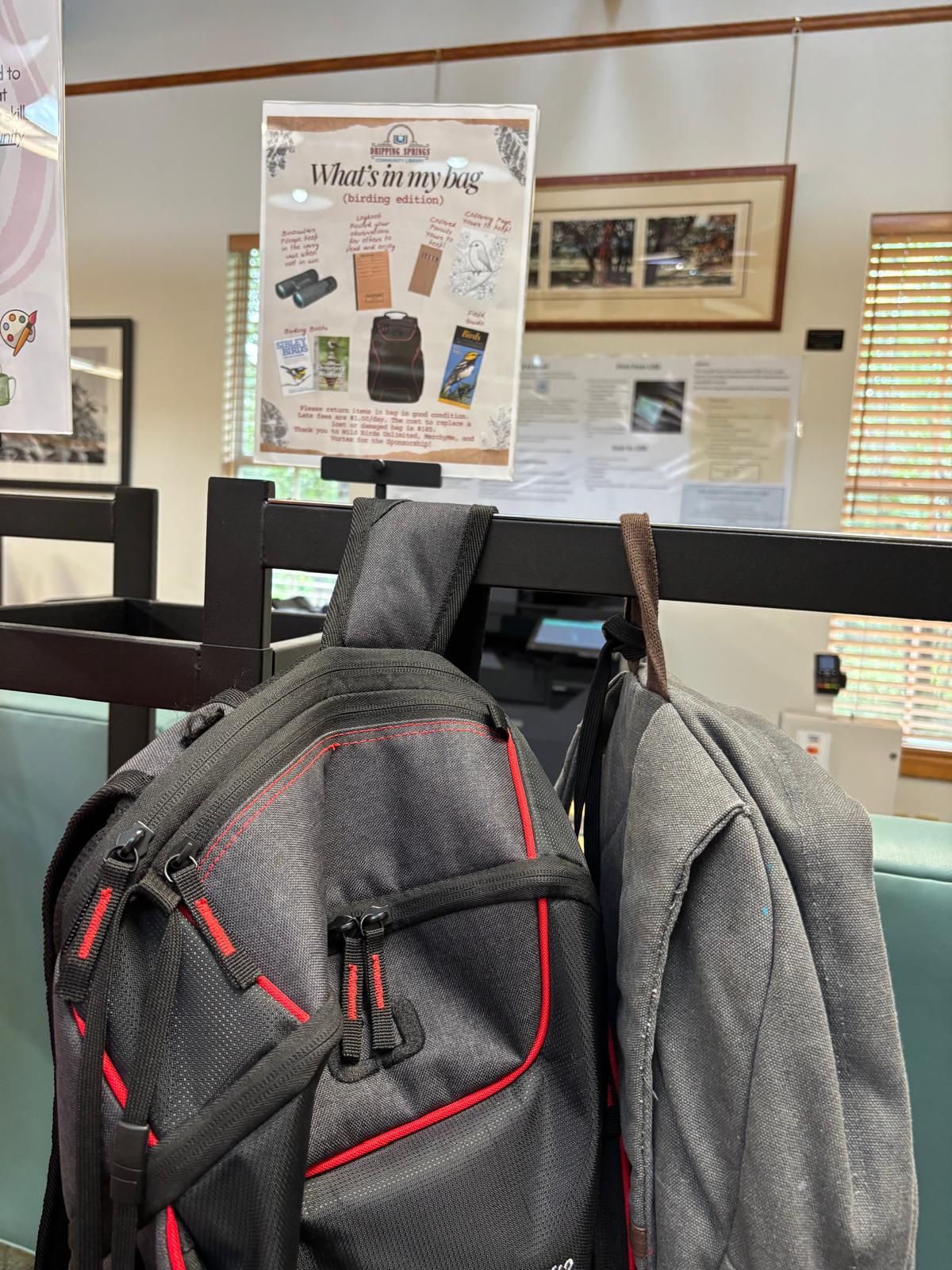 Backpacks hung on a chair at the library, under a "What's in my bag" poster