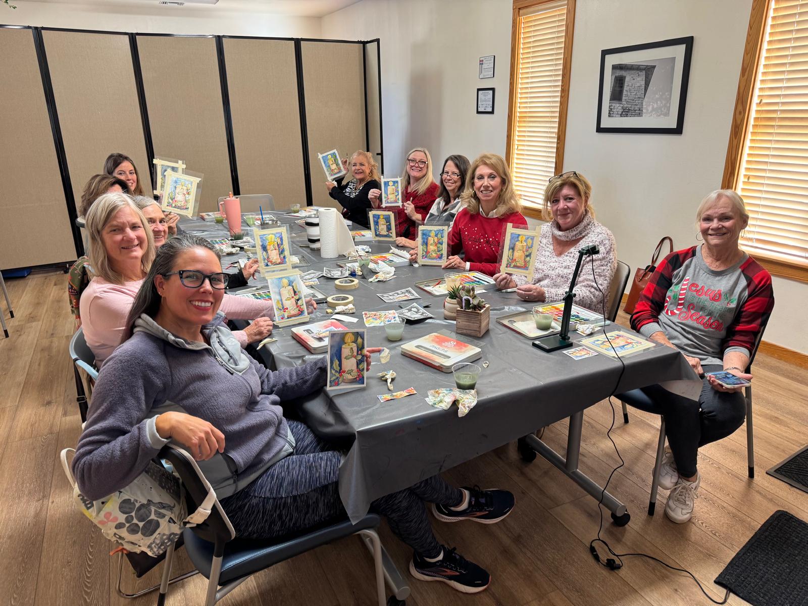 People around a long table in the library holding up small paintings they made at a class
