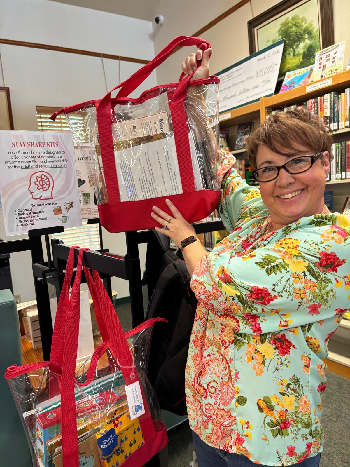 A volunteer in the library holding up a clear red-trimmed tote bag packed with supplies