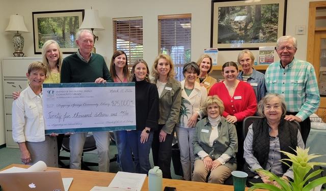 A group of people in the library, two of them holding a large donation check