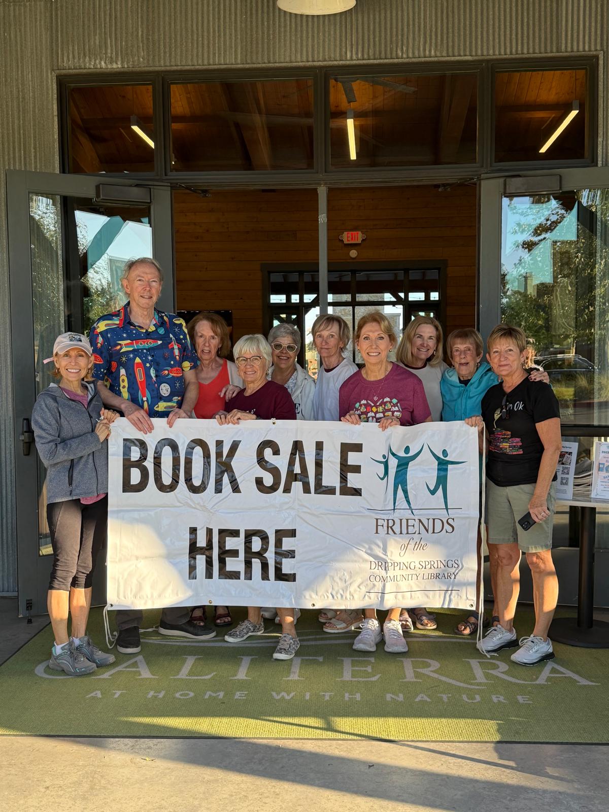 A group of volunteers holding a Friends banner that reads Book Sale Here