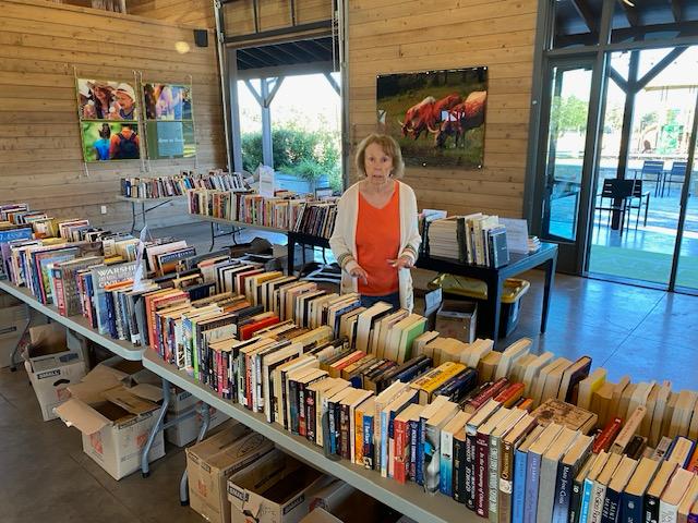 A volunteer standing behind long tables of donated books, sorted spine-up for a sale